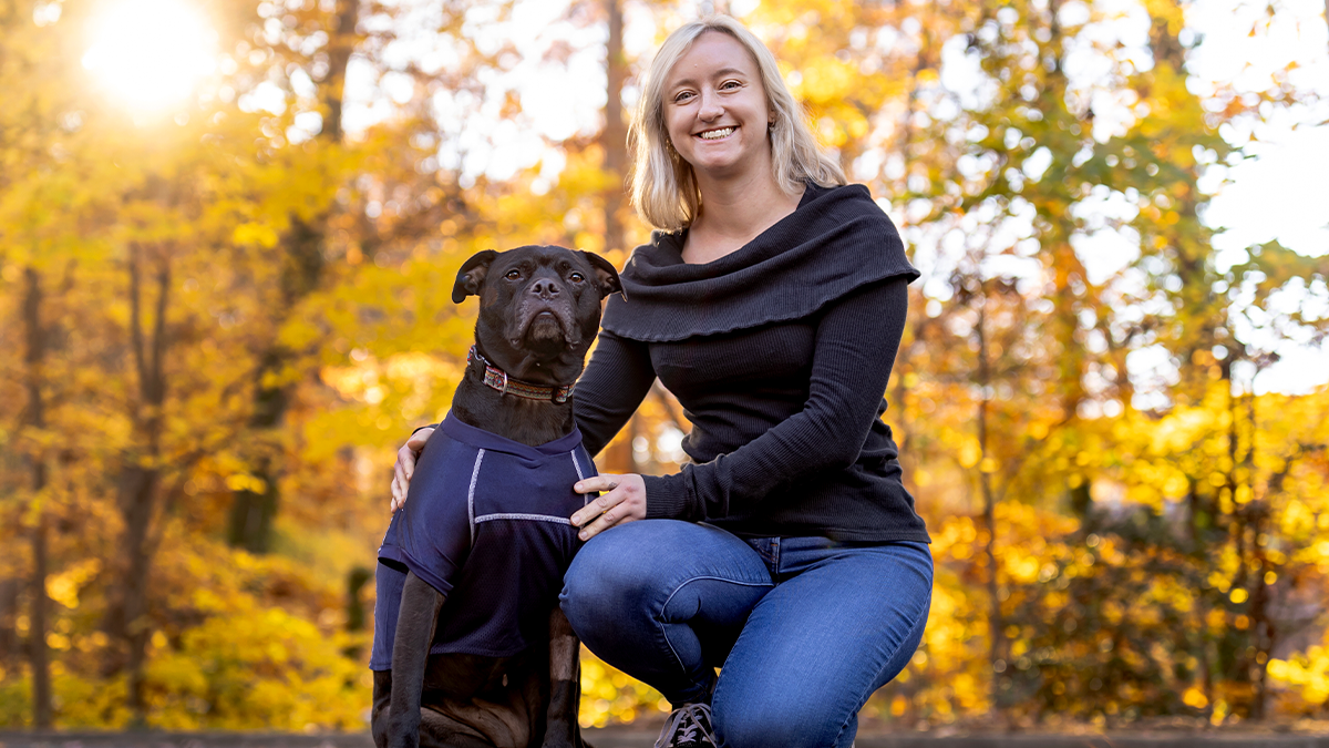 Caitlin Russell posing with her dog, Lumen against autumnal backdrop.